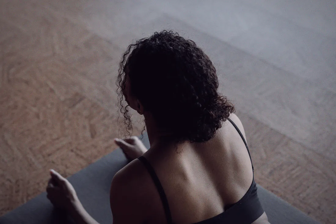 Seen from behind, a student rests forward on a mat in soft light during a restorative class.