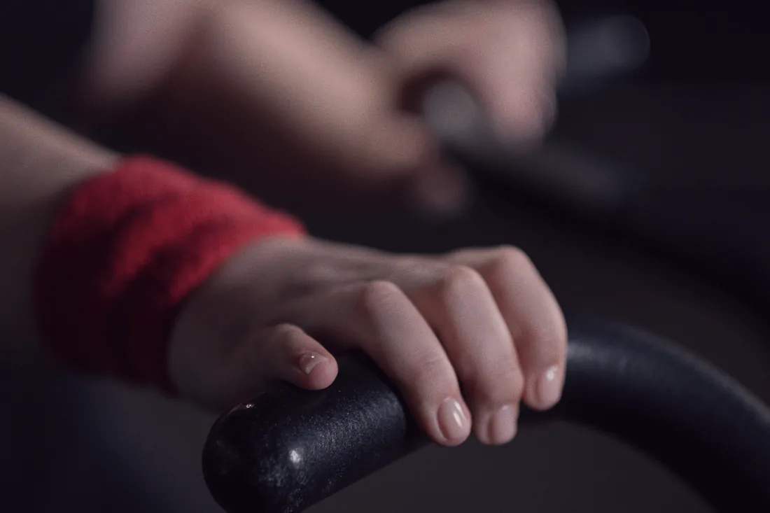 Two hands grip the handlebars of a studio bike in warm, low light during a ride class.