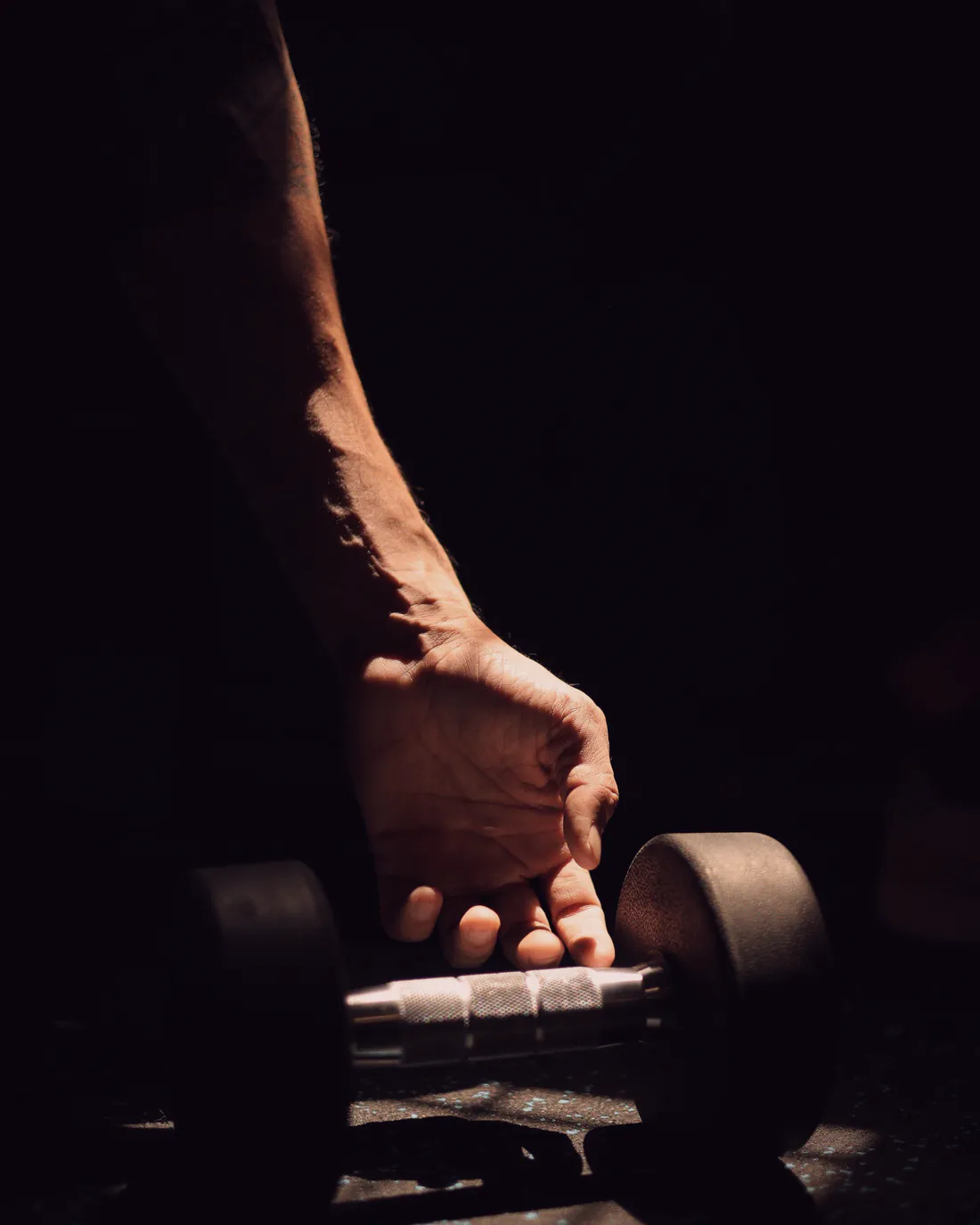A hand closes around a dumbbell in low, warm light during a strength class.