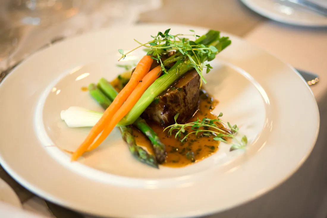 A plated fillet with glazed baby carrots, asparagus and jus, finished with microgreens.