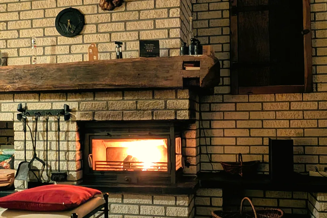 A wood-burning fire glowing in a brick fireplace with a reclaimed-timber mantel.