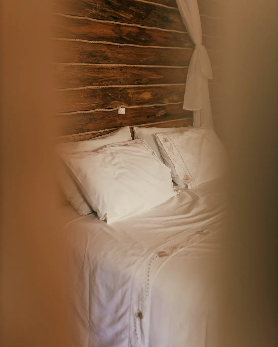 A guest bedroom with white linen and a reclaimed-timber headboard in soft, warm light.