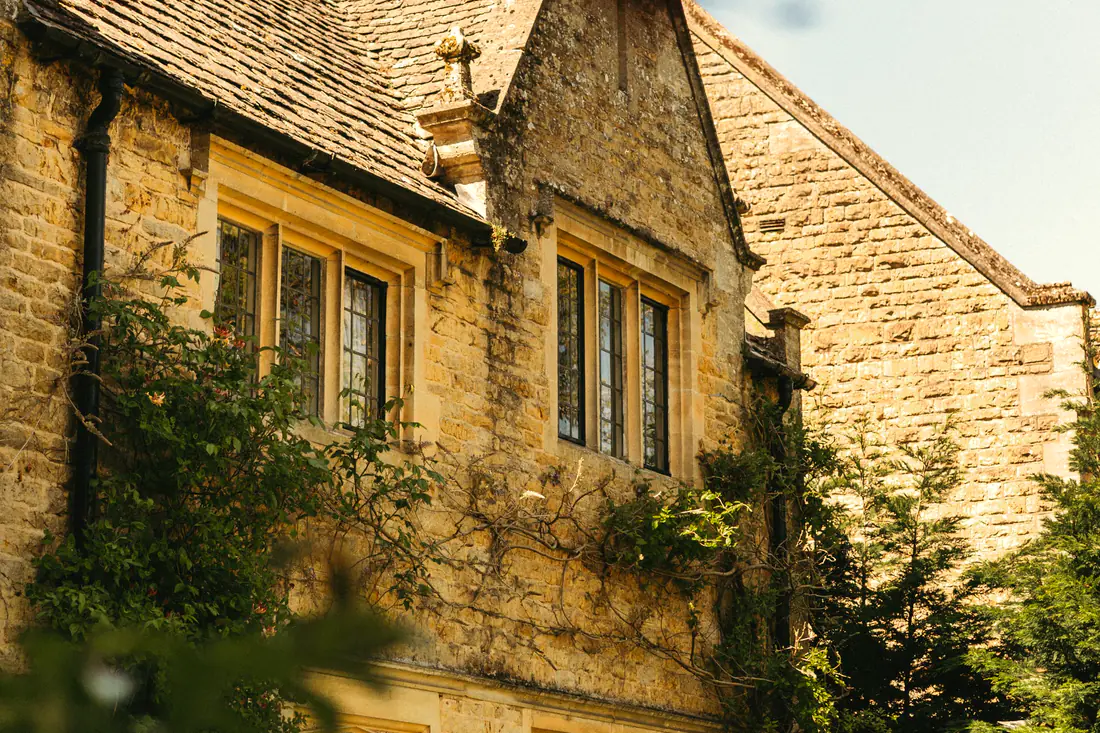 The honey-stone country house and its clipped garden, warm in late-afternoon sun.